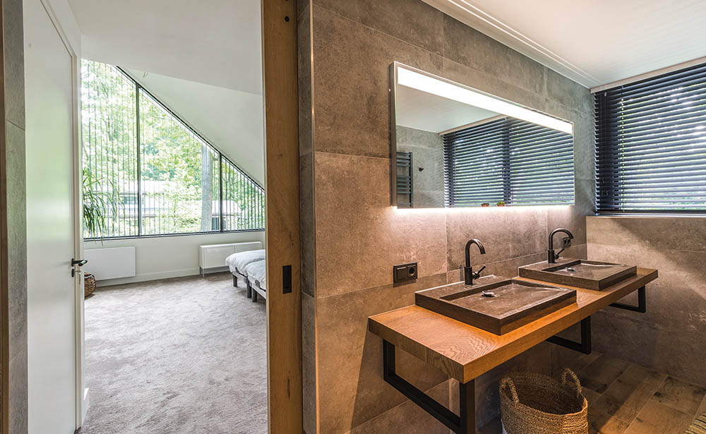Door de combinatie van beton, natuursteen en hout is er ook in de badkamer een balans tussen modern en landelijk